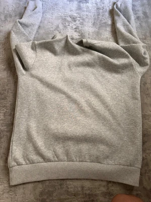 Grå hoodie från Stone Island  - Säljer en stilren grå hoodie från Stone Island med den klassiska svarta och gula loggan på ärmen. Hoodien har huva och ribbade muddar vid ärmslut och nederkant. Tillverkad i mjukt bomullsmaterial som är skönt att bära.