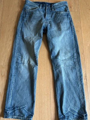 Blå raka jeans med detaljer - Säljer ett par klassiska blå jeans med raka ben och coola sömdetaljer vid knän och benslut. Jeansen har fem fickor och bälteshällor. Materialet är denim i 100% bomull. Perfekta för en avslappnad och trendig stil.
