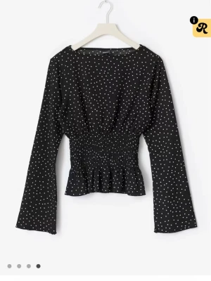 Svart prickig blus med volang💕 - Snygg svart Gina tricot  blus med vita prickar och smockad midja som ger en markerad siluett. Blusen har långa ärmar och volang nedtill för en trendig look. Perfekt att styla med både jeans och kjol. Fint skick och pris kan alltid diskuteras 💕