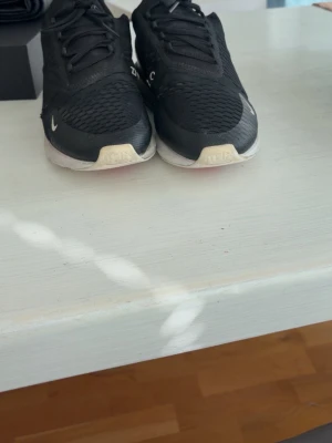 Svarta Nike sneakers med meshdetaljer - Säljer ett par svarta Nike sneakers med meshdetaljer och vita samt röda inslag på sulan. Skorna har en sportig look med lågt skaft och snörning. Perfekta för dig som gillar streetwear och vill ha bekväma skor till vardags.