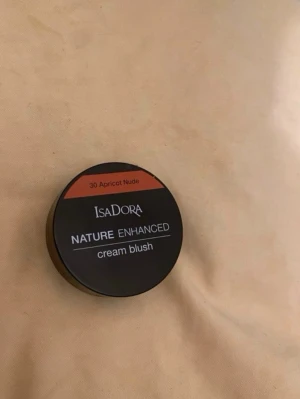 Isadora Nature Enhanced Cream Blush - Krämrouge från Isadora i nyansen 30 Apricot Nude. Kommer i en rund svart dosa med spegel i locket. Färgen är en varm aprikos-ton som ger ett naturligt glow till kinderna. Perfekt för dig som gillar en fräsch och naturlig look.