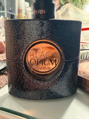 Yves Saint Laurent Black Opium EdP - Black Opium Eau de Parfum från Yves Saint Laurent är en ikonisk parfym i en svart, glittrig flaska med rundad form och kopparfärgad detalj. Doften är djärv och sensuell, perfekt för dig som vill sticka ut. Flaskan rymmer 50 ml och har en lyxig design. Endast testat, säljes då den inte används 