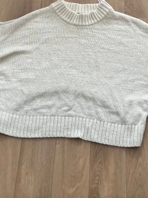 Ljusgrå stickad poncho - Säljer en ljusgrå stickad poncho med ribbad hög krage och bred ribbad kant nedtill. Ponchon har en lös och boxig passform, perfekt att slänga över en tröja för extra värme. Materialet känns mjukt och bekvämt. Den hade passat med vit linne under och svarta costym byxor. 