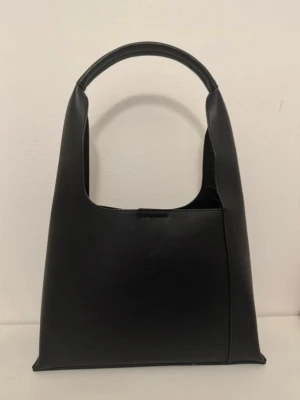 Svart stilren handväska  - Stilren handväska från Even & Odd, passar både till fest och vardag. Använd fåtal gånger  Höjd: 21 cm Längd: 30 cm  Vidd: 10.5 cm  Handtag: 23 cm 