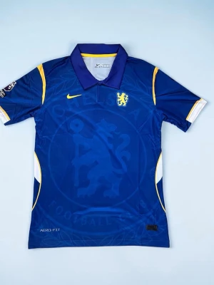 chelsea Blå fotbollströja med krage - Har också en L om du vill ha. Snygg blå fotbollströja från Nike med krage och gula detaljer. Tröjan har ett gult lejonmärke på bröstet, gul Nike-logga och diskreta mönster i tyget. Tillverkad i Dri-FIT material som andas, perfekt för träning eller match.