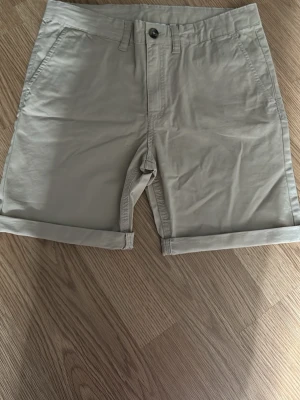 Beige bomullsshorts med uppvik - Snygga beige shorts i bomull med klassisk passform och uppvikta benslut. Shortsen har sidofickor fram, två bakfickor och stängs med knapp och dragkedja. Perfekta för varma dagar och enkel att matcha med olika stilar.