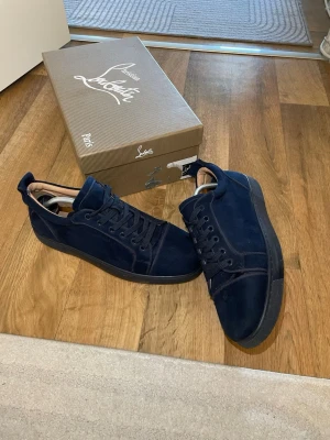 Mörkblå mockasneakers från Louboutin - Snygga mörkblå sneakers i mocka från Louboutin med klassisk låg profil och svarta sulor. Skorna har matchande mörkblå skosnören och diskreta sömdetaljer. Perfekta för dig som vill ha en stilren och exklusiv look. 