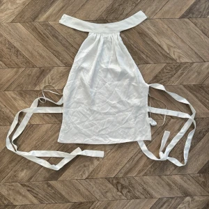 Vit halterneck linnetopp från Zara - Säljer en vit halterneck linnetopp från Zara med knytband i ryggen. Toppen har en stilren och minimalistisk design, perfekt för att skapa en trendig look. Materialet känns lätt och svalt, vilket gör den skön att bära under varma dagar.