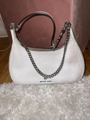 Michael Kors Piper Small Pebbled Leather Shoulder Bag i vitt. - Väldigt fin och klassisk väska som fortfarande är hel och fungerar perfekt. Den har använts i några år och har därför fått naturliga användningsspår på det ljusa lädret, framför allt lite mörkare/gråaktiga skuggningar på vissa delar av väskan. Inga trasiga delar eller större skador, endast kosmetiska spår från användning.  Säljer den då jag inte använder den längre.