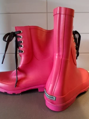 Rosa gummistövlar Vagabond Storlek 36 - Säljer ett par coola rosa gummistövlar med svarta snören och grov sula. Stövlarna har en klassisk form och är perfekta för regniga dagar. Stövlarna är använda och har lote skavanker som kan ses på bilder. Men ör fortfarande fina.