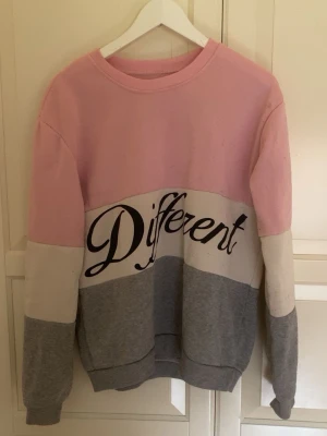 Rosa, vit och grå tröja med text - Säljer en oversized sweatshirt i färgblock med rosa upptill, vitt i mitten och grå nedtill. Stor text 'Different' tryckt över bröstet. Tröjan har rund halsringning, långa ärmar och mjukt material, perfekt för en chill och avslappnad stil.