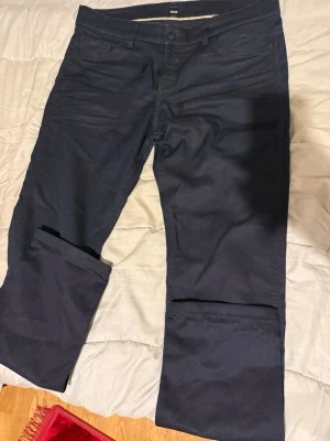Mörkblå chinos från BOSS - Snygga mörkblå chinos från BOSS i klassisk rak modell. Tillverkade i mjukt bomullsmaterial med diskreta fickor fram och bak. Perfekta för en clean och stilren look. Passar dig som gillar enkel men exklusiv stil.