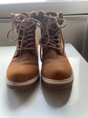 Bruna kängor från Fila med snörning - Säljer ett par snygga bruna kängor från Fila med grov snörning och vadderad kant. Kängorna har en robust sula i vitt och brunt samt metallhål för snörena. Perfekta för höst och vinter!😊