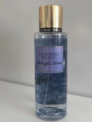 Victoria's Secret Midnight Bloom mist - Fräsch och blommig body mist från Victoria's Secret i doften Midnight Bloom. Flaskan är genomskinlig med blått innehåll och har ett elegant guldigt lock. Volymen är 250 ml och flaskan är av plast. Doften har inslag av moon flower och creamy woods.