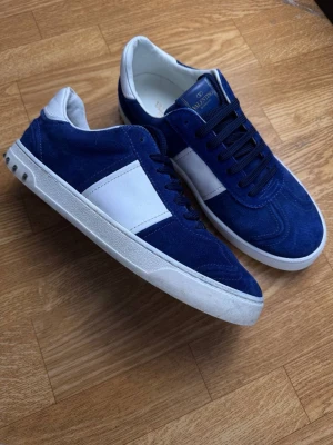 Blåa sneakers från Valentino - Snygga blåa sneakers från Valentino med vit detalj på sidan och vit sula. Ovandelen är i mocka och skorna har svarta skosnören. Insidan och hälen är vita för en clean kontrast. Perfekta för dig som vill ha en stilren och trendig look.