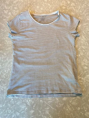 Randig t-shirt från H&M Basic - Kortärmad t-shirt från H&M Basic i vitt med tunna svarta ränder. Tillverkad i mjuk bomull och har en klassisk rund halsringning. Perfekt för en avslappnad och enkel stil.