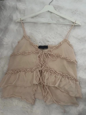 Beige linnetopp med volanger och snörning - Supersöt beige linnetopp med tunna axelband, volangdetaljer och snörning framtill. Inprincip oanvänd från Zara. Storlek: S Pris: 220kr