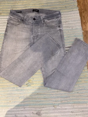 Jack & Jones jeans slimfit grå - Säljer ett par ljusgrå slim fit jeans från Jack & Jones, modell Glenn. Jeansen har en defekt vid bakfickan (se bild). Riktiga sköna o stretchiga jeans i en snygg färg. Priset e inte spikat!