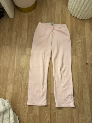 Ljusrosa mjukisbyxor med dragsko - Säljer ett par ljusrosa mjukisbyxor med rak passform och dragsko i midjan. Byxorna är tillverkade i ett mjukt och bekvämt material, perfekta för chill dagar hemma eller när du vill vara extra comfy.