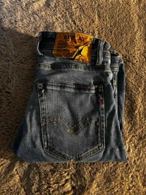 Ljusblå jeans från Replay, storlek 28 - Säljer ett par ljusblå jeans från Replay i storlek 28. Klassisk femficksmodell med snygga kontrastsömmar och Replay-logga på bakfickan. Jeansen har en avslappnad passform och är tillverkade i mjukt denimtyg. Lite slitna men funkar perfekt, säljer pga att de är för små!