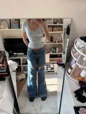 Ljusblå randig topp - Säljer en ljusblå och vit randig topp med korta ärmar. Toppen har rundad, djup ringning och är ribbad i materialet vilket ger en snygg och bekväm look. Perfekt till jeans eller kjol för en trendig stil. Storlek xs! 