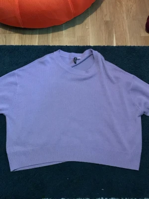 Ljuslila cropped stickad tröja - Säljer en ljuslila stickad tröja med croppad passform och rund hals. Tröjan har  ribbade kanter nedtill och vid halsen. Perfekt för dig som gillar en avslappnad och trendig stil.
