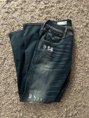 Blå slitna jeans från Replay - Säljer ett par blå jeans från Replay med snygga slitningar och tvättade detaljer framtill.  Storlek 32,32