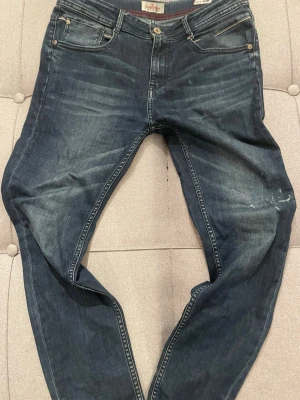 Mörkblå slim jeans från Vingino - Snygga mörkblå slim fit jeans från Vingino med klassisk femficksmodell och diskreta slitningar. Jeansen har röda sömdetaljer och en liten italiensk flaggdetalj vid fickan. Perfekta för dig som gillar en smalare passform och stilren look.