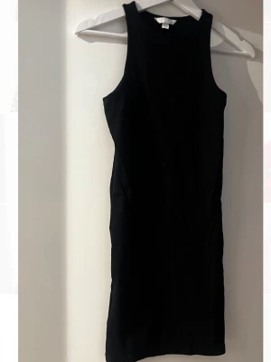 Svart ribbad ärmlös klänning H&M - Snygg svart ribbad klänning från H&M i kort modell. Klänningen är ärmlös med rund halsringning och har en tight passform.