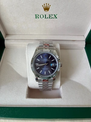 silverfärgad Datejust klocka - Ny Datejust i silver med blå urtavla, komplett med originalförpackning. Urtavla på 41 mm. Automatiskt urverk. Nattbelysningsfunktion🎇Perfekt för dig som älskar lyxiga accessoarer.