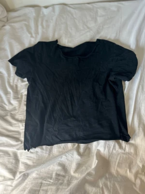 Svart t-shirt med snörning i ryggen - Cool svart t-shirt i bomull med korta ärmar och unik snörningsdetalj i ryggen. Perfekt för dig som vill ha en edgy och personlig stil. Passformen är normal och tyget är mjukt och bekvämt.
