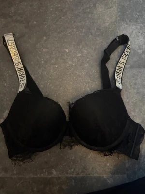 Svart push-up bh med spetsdetaljer - Säljer en Snygg svart push-up bh från Victoria secret med vadderade kupor och spetsdetaljer längs kanterna. Perfekt för dig som vill ha något extra till underklädesgarderoben. Nytt skick aldrig använd !!! Nypris 1200kr