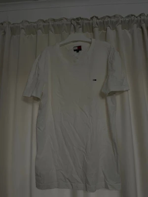 Vit t-shirt från Tommy Hilfiger - Klassisk vit t-shirt från Tommy Hilfiger med liten logga på bröstet. T-shirten har rund halsringning och korta ärmar. Tillverkad i mjuk bomull för en skön känsla och enkel stil som funkar till allt.