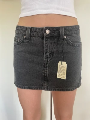 Svart jeanskjol från Levi's - Snygg svart jeanskjol från Levi's i klassisk femficksmodell. Kjolen har bälteshällor, knapp och dragkedja framtill samt en rak, kort passform. Perfekt att matcha med en crop top eller hoodie för en cool vardagslook. Helt ny med prislappar. Nypris ca 700-800kr