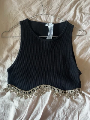 Svart ribbad croppad topp med diamanter  - Trendig svart ribbad croppad topp från Zara med ärmlös design och snygga pärldetaljer längs nederkanten. Perfekt för dig som vill sticka ut med en unik detalj. Materialet känns mjukt och stretchigt.