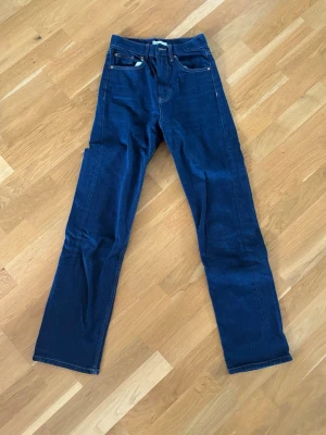 Mörkblå raka jeans med hög midja - Säljer ett par mörkblå jeans med rak passform och hög midja. Klassisk femficksmodell med dragkedja och knapp framtill. Jeansen har kontrastsömmar och är tillverkade i ett kraftigt denimtyg. Perfekta för en clean och tidlös look.