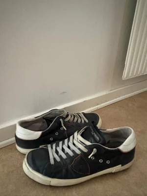 Philippe model skor - Snygga låga sneakers i svart läder med vita detaljer och vita skosnören. Skorna har en klassisk siluett med kontrasterande vit sula och hälparti. Passar perfekt till streetwear och casual outfits.