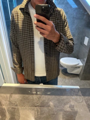 Brunrutig overshirt med krage - Säljer nu en riktigt schysst skjorta som även funkar som overshirt. Schysst skjorta som passar året runt även nu på sommaren. Det finns inga skador och skjortan är i riktigt bra skick utan några skador. Jag på bilden är 188cm. Hör av er vid fler frågor och eventuella prisförslag:)