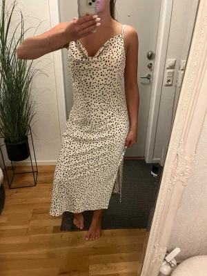 Långklänning  - Säljer en vit midiklänning med svarta prickar och tunna axelband. Klänningen har en draperad urringning och en slits på vardera sidan som ger en snygg detalj. Materialet ser ut att vara mjukt och följsamt, perfekt för sommarens alla tillfällen. Denna är en storlek 42 men passar mig som vanligtvis är 36 för en luftigare look.