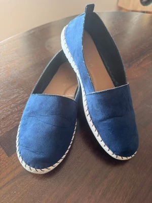 Mörkblå slip-on skor i mockaimitation - Snygga mörkblå slip-on espadrillos med ovandel i mockaimitation och vit gummisula med dekorativa sömmar. Skorna har en enkel och stilren design som passar till många olika outfits, inte minst till långklänningen i blått som jag också säljer just nu!