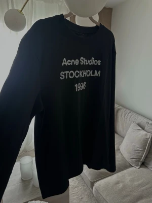 Svart långärmad Acne Studios t-shirt - Säljer en svart långärmad t-shirt Acne Studios med tryck i vitt framtill där det står 'Acne Studios STOCKHOLM 1996'. Skön passform och klassisk rund hals. Perfekt för dig som gillar stilrena plagg med en twist.