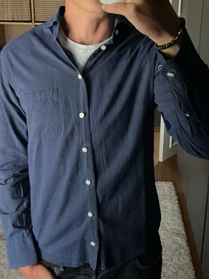 Eton skjorta i mörkblå - stl 40 (M) - 100% bomull med små prickar vävda i tyget. Slim fit med bröstficka, funkar till både jeans och kostymbyxor. Personen på bilden är 189cm, väger 78kg.  Använd men i mycket bra skick, inga hål eller fläckar. En knapp vid ena ärmslutet är annan färg, detta är original, syns på bild.  Rök- och djurfritt hem. Skriv gärna om du vill ha fler bilder eller undrar något!