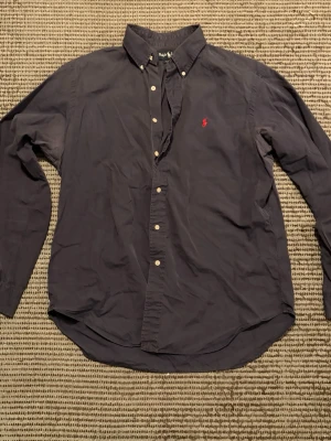 Ralph Lauren skjorta - Fin men använd skjorta i bra skick från Ralph Lauren, mörklblå med den klassiska röda Polo loggan! Storlek L med lite avslappnande fit vilket gör så att den ser stekhet ut på stranden! vill ni se med bild på så löser jag såklart det! bara att skicka ett PM vid vidare frågor!!!
