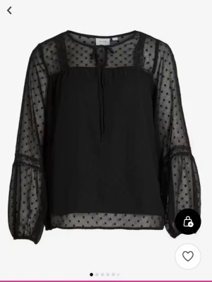 Svart  blus med prickar - Snygg svart blus från Vila med transparenta, prickiga långärmar och detaljer i spets. Blusen har rund halsringning med knytband och är gjord i ett lätt, luftigt material som ger en trendig look.