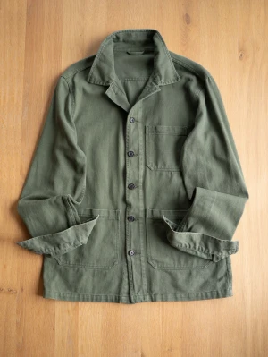 Green Chore Jacket, size M - Stilren olivgrön overshirt i kraftigt bomullstyg. Klassisk krage, knäppning med svarta knappar och tre utanpåliggande fickor framtill. Perfekt lager-på-lager-plagg med avslappnad passform och uppvikta ärmar för en casual look.