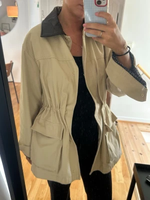 Beige jacka med läderkrage - Strl S - Säljer en superfin och trendig jacka från H&M (Divided) i beige canvasmaterial!  - Storlek: S (passar även XS/M beroende på hur du vill att den ska sitta, lite oversize modell) - Detaljer: Mörkbrun krage i skinnimitation (läderlook), rutigt foder som syns snyggt nar man viker upp armarna, stora fickor fram samt dragsko i midjan för att justera passformen. - Skick: Sparsamt använd utan anmärkningar Superfin till både höst och vår!
