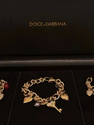 Dolce & Gabbana smyckeset  - Smyckeset – mycket lägre pris på Plick än hos Vestiaire. Fantastiska statement pieces från Dolce & Gabbana i guldpläterad metall med pärlor och små hjärt- och nyckelberlocker. Armband och örhängen med grov kedja och karbinlås. Öppen för seriösa bud.
