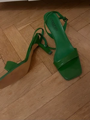 Gröna sandaletter med klack - Snygga gröna sandaletter från Boohoo med fyrkantig tå och smal rem över foten. Skorna har en medelhög blockklack och justerbar ankelrem. Tillverkade i ett glansigt material som ger en trendig look.