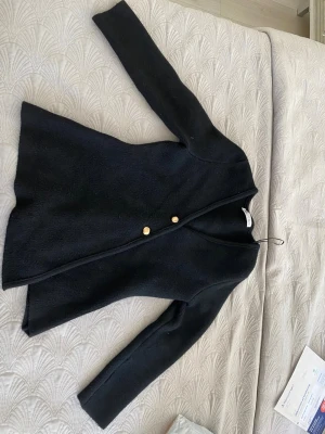 Svart kappa med guldknappar - Stilren svart kappa med två guldknappar framtill. Kappan har en rak och något figursydd passform, lång ärm och enkel design utan krage. Osymmetrisk kappa Perfekt för kyligare dagar.❤️
