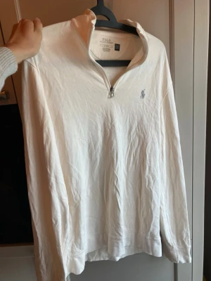 Tröja Polo Ralph Lauren - Klassisk beige långärmad tröja från Polo Ralph Lauren med halv dragkedja och broderad logga på bröstet. Tillverkad i mjuk bomull och har en avslappnad passform. Perfekt för en clean och stilren look. Strl:M